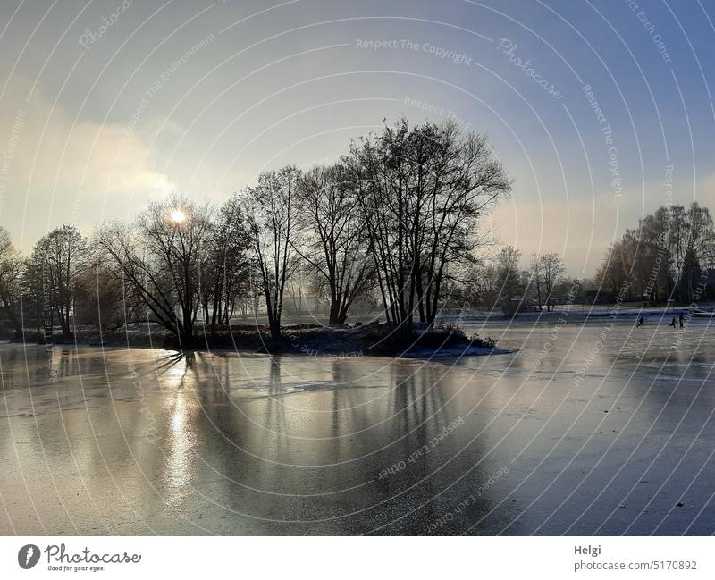 eiskalte sonnige Winterstimmung am zugefrorenen See, im Hintergrund ganz winzig drei Schlittschuhläufer Kälte Eis Eisfläche Sonnenlicht Licht Schatten