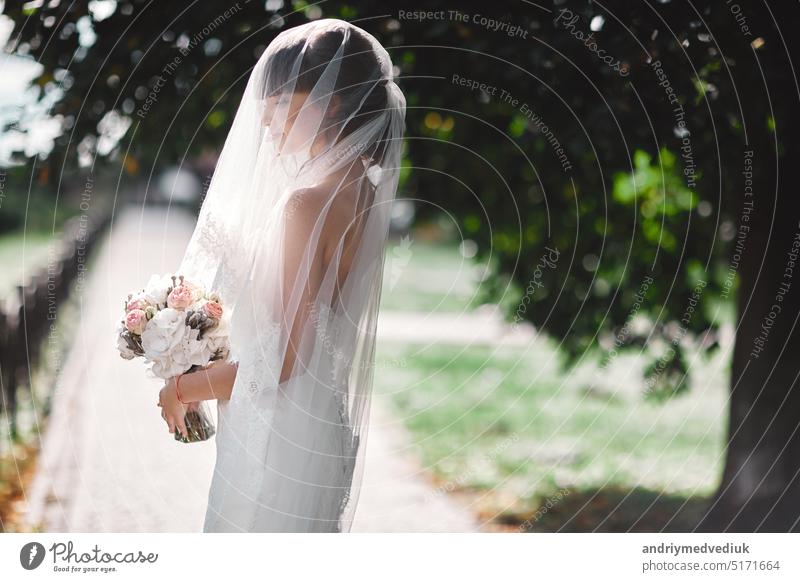 Schöne Braut im Brautkleid mit Blumenstrauß und Spitzenschleier auf die Natur. Schönes Modell Mädchen in einem weißen Hochzeitskleid. Weibliches Porträt im Park. Frau mit Frisur. Niedliche Dame im Freien