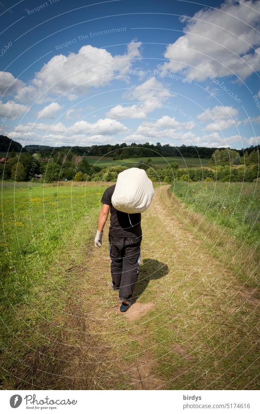 Rückansicht eines Mannes mit Gepäck auf der Schulter. Mann geht einen Feldweg entlang schleppen Seesack tragen Natur weggehen Landschaft Horizont schönes Wetter