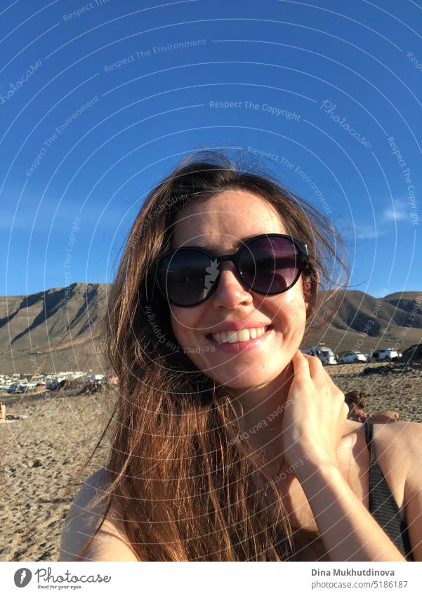 Selfie eines Mädchens mit Sonnenbrille. Junge Frau entspannt im Urlaub, stehen am Strand in der Nähe von Bergen, in Sonnenuntergang Licht, lächelnd. Echte Menschen. Authentisches Bild von echten Menschen.