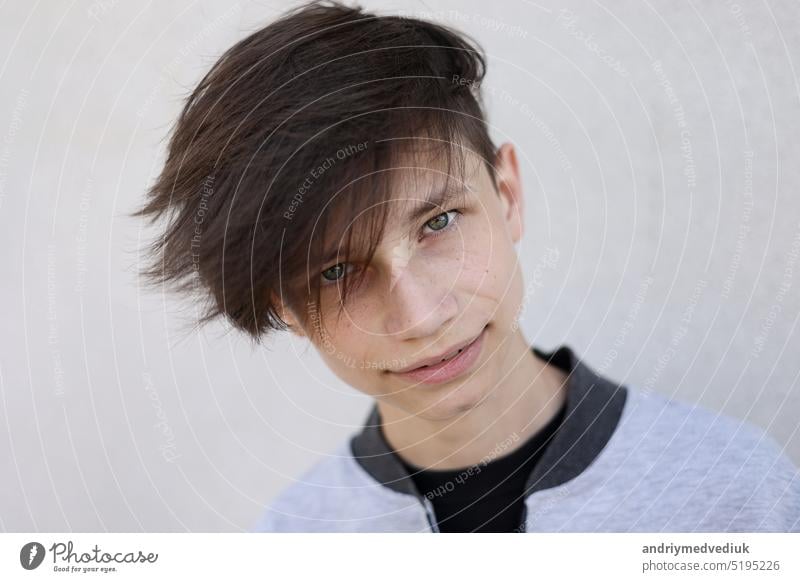 Schöner junger Mann mit stilvollem Haarschnitt. Porträt von Teenager-Junge mit Jugendfrisur steht auf grauem Hintergrund und schaut in die Kamera. Gesicht
