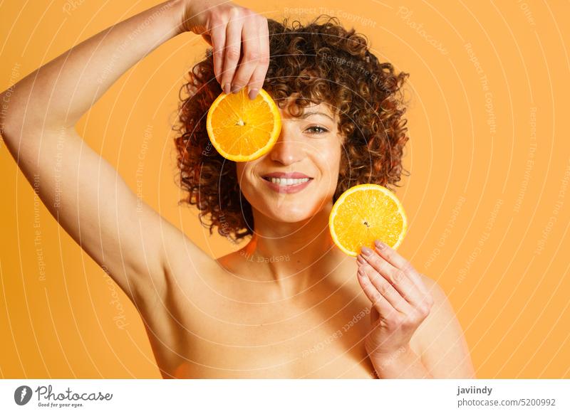 Heiteres weibliches Modell mit Orangenscheiben Frau orange Lächeln Hautpflege Vitamin C Auge abdecken Spa Scheibe hell Farbe Monochrom Zitrusfrüchte frisch