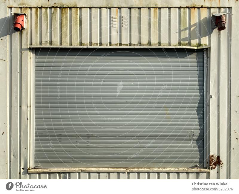 Geschlossener Rollladen eines Baucontainers im Sonnenlicht Fenster geschlossen alt abgenutzt Baustelle Container Bürocontainer schmutzig Fassade grau