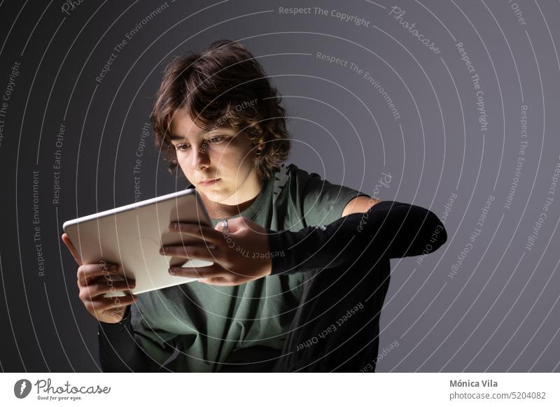 Ein junges Mädchen surft mit einem Tablet oder einem elektronischen Gerät in einem schwach beleuchteten Raum im Internet Teenager T-Shirt dunkel grau schwarz