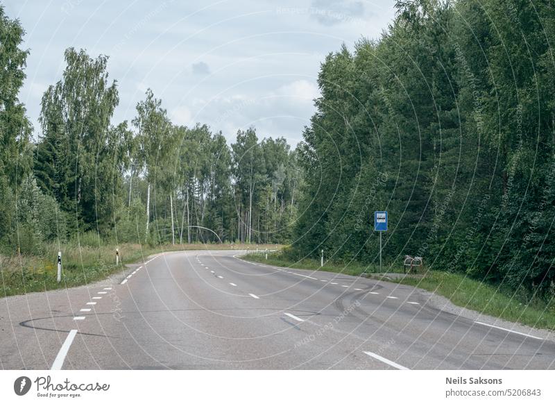 leere Asphaltstraße in grünem Sommerwald mit Bäumen und Gras. Perspektive, Bushaltestelle in Lettland Landschaft Hintergrund schön blau Blauer Himmel Kurve