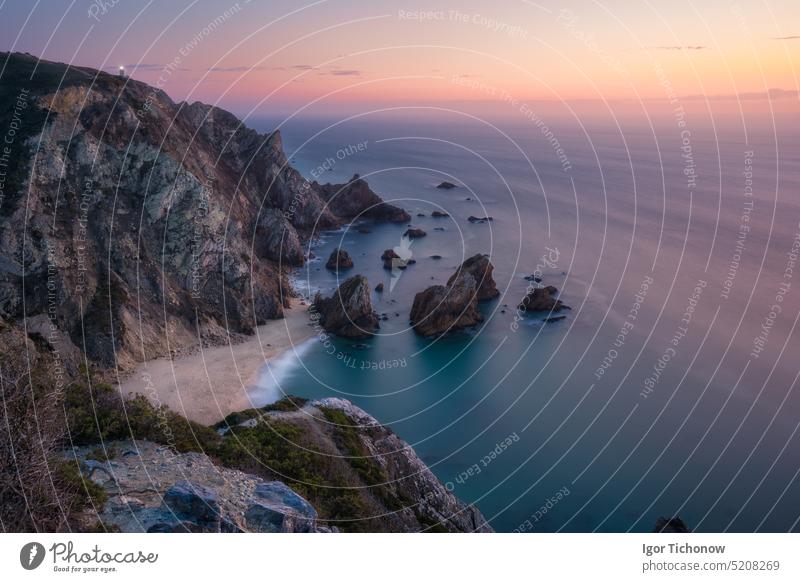 Sonnenuntergang über dem versteckten surrealen Strand Praia Da Ursa. Cabo Da Roca mit Leuchtturm im Hintergrund. Atlantikküste, Portugal, Europa Abenddämmerung