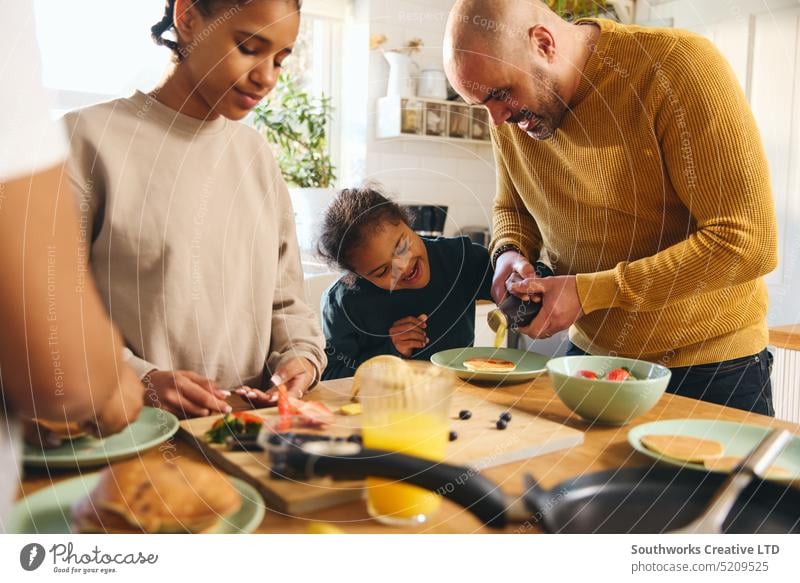 Junge mit Down-Syndrom isst Pfannkuchen zum Frühstück mit seiner Familie rassenübergreifend dienen essen eingießen Sirup Eltern vier schwarz Küche Lebensmittel