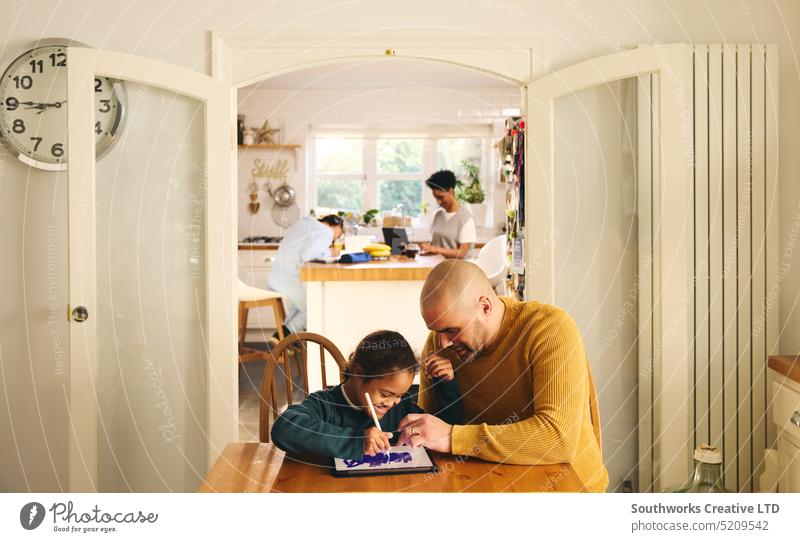 Multirassische Familie zu Hause mit Vater und Sohn mit Down-Syndrom, die ein digitales Tablet benutzen heimwärts digitales Tablett Lifestyle zeichnen