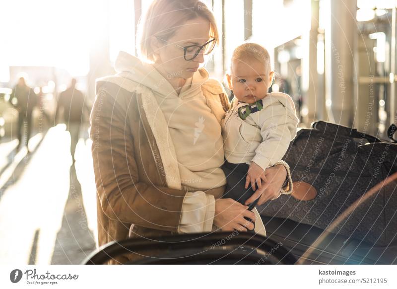 Motherat Reisen mit seinem Säugling Junge Kind, zu Fuß, Schieben Kinderwagen und Gepäckwagen vor dem Flughafen-Terminal Station. reisen Baby Urlaub Ausflug