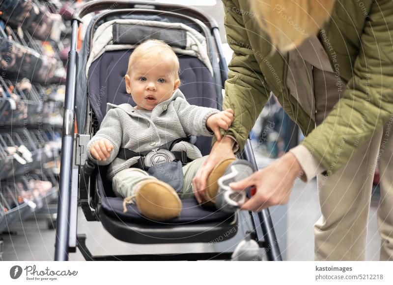 Casualy gekleidet Mutter Auswahl sportlicher Schuhe und Kleidung Produkte in Sport-Abteilung des Supermarktes mit ihrem Säugling Junge Kind im Kinderwagen. Frau