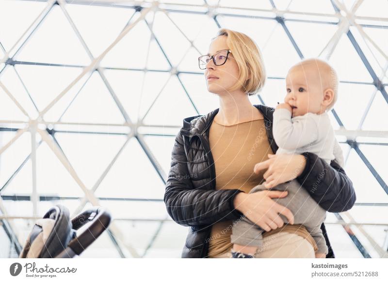 Mutter carying sein Baby Junge Kind, schieben Kinderwagen am Flughafen Abflugterminal warten an Bord Gates ein Flugzeug zu besteigen. Familie reisen mit Baby-Konzept.