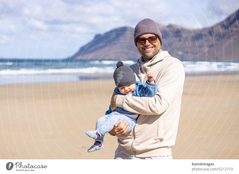 Vater genießt die reine Natur und spielt mit seinem kleinen Sohn am windigen Sandstrand von Famara, Insel Lanzarote, Spanien. Familie Reisen und Elternschaft Konzept.