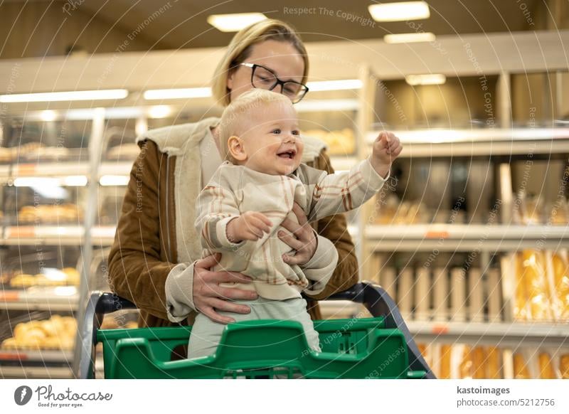 Eine Mutter kauft mit ihrem kleinen Jungen ein und hält das Kind, während sie an der Kasse im Supermarkt Produkte stapelt. Frau Baby Säugling Mama Laden kaufen