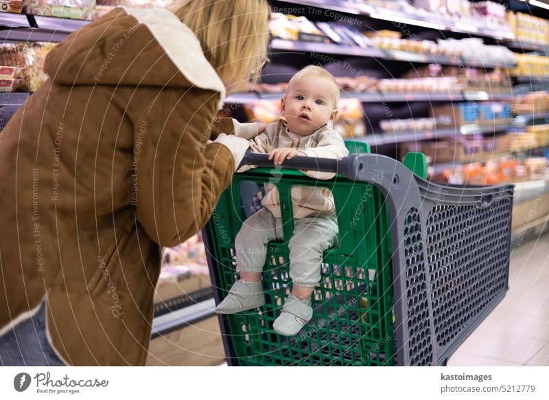 Eine Mutter kauft mit ihrem kleinen Jungen ein und hält das Kind, während sie an der Kasse im Supermarkt Produkte stapelt. Frau Baby Säugling Mama Laden kaufen