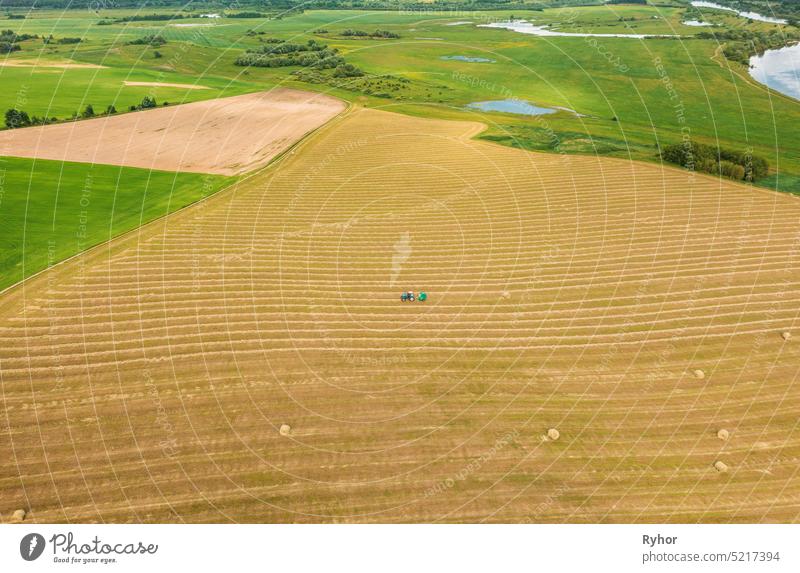 Luftaufnahme Traktor sammelt trockenes Gras in Strohballen im Weizenfeld. Spezielle landwirtschaftliche Ausrüstung. Heuballen, Heu machen.