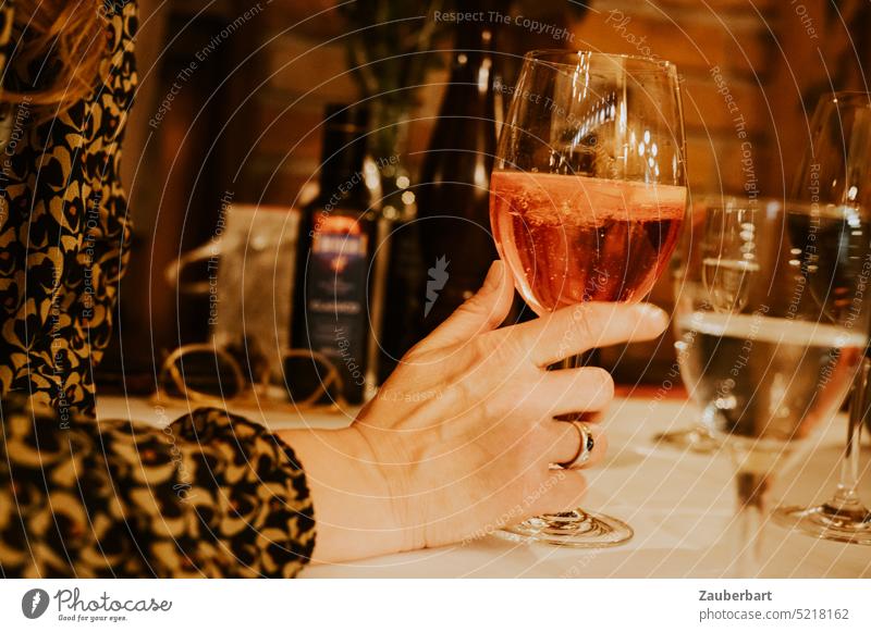 Hand hält Glas mit rotem Getränk, davor Weinglas, an Tisch im Restaurant in abendlicher Beleuchtung Spritz Ring Italiener Finger Abend feiern trinken Gäste