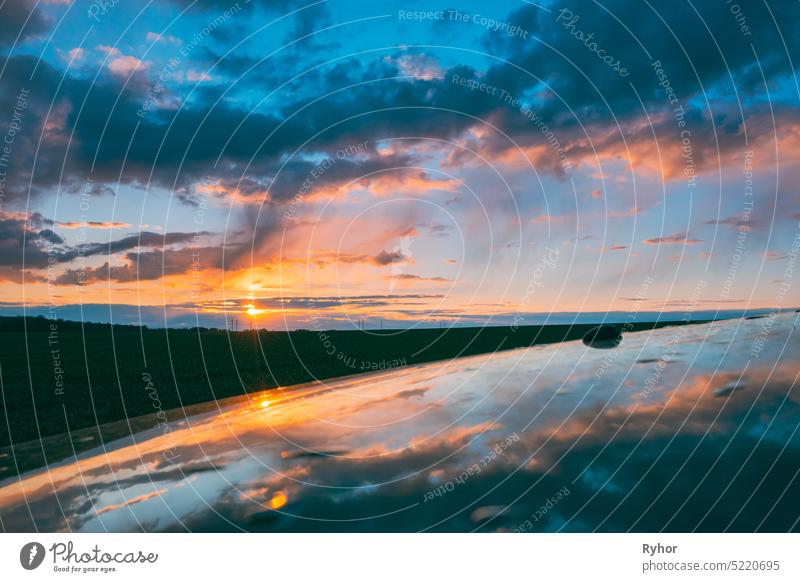 Sonnenuntergang Himmel mit untergehender Sonne reflektiert in Motorhaube des Autos. Landschaft auf dem Lande unter Scenic bunten Himmel bei Sonnenuntergang Dämmerung Sonnenaufgang. Skyline