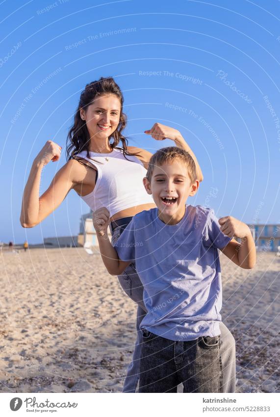 Glückliche Mutter und Sohn Zeigen starke Arme am Strand in einem sonnigen Tag am sonnigen. Familie zusammen spielen MEER Sonnenuntergang im Freien Kleinkind