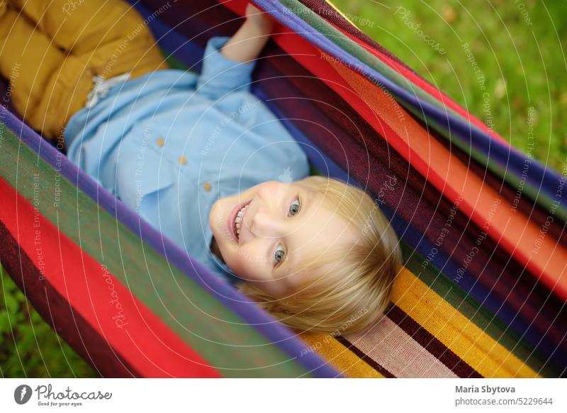 Nette kleine blonde weiße Junge genießen und Spaß haben mit bunten Hängematte im Hinterhof oder Spielplatz im Freien. Sommer im Freien aktive Freizeit für Kinder. Kind