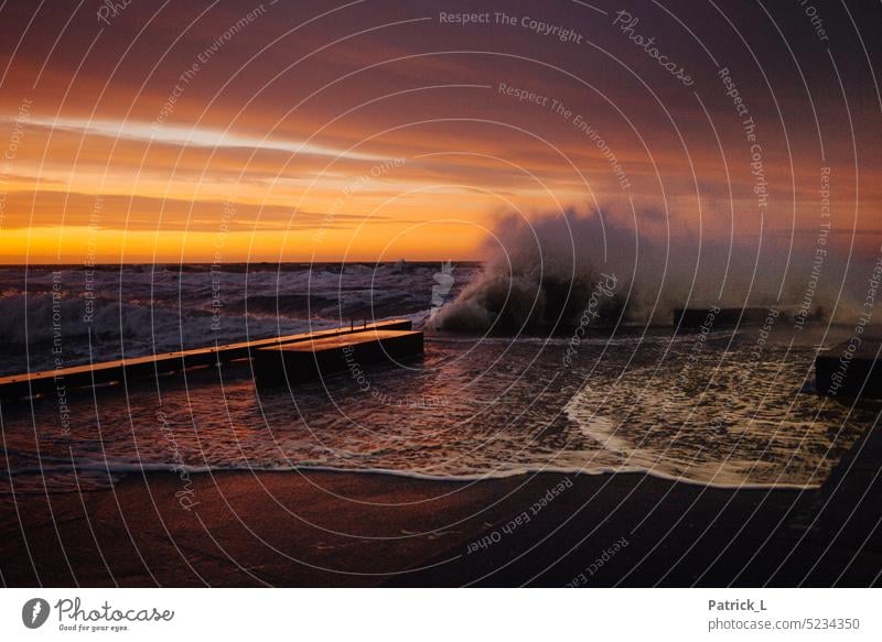 Eine Welle bricht an einer Mole im Sonnenuntergang Wellen Wasser Meer Nordsee warm farbe wolken menschenleer kraft wind Wellengang Dänemark Macht Naturgewalt