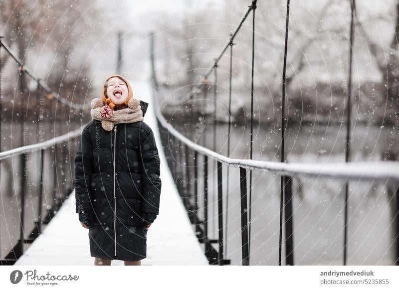 Lustiges kleines Mädchen fängt Schneeflocken in einem schönen Winterpark während eines Schneefalls. Süßes Baby spielt im Schnee. Winter-Aktivitäten für Kinder. die Winterferien. glückliche Kindheit.