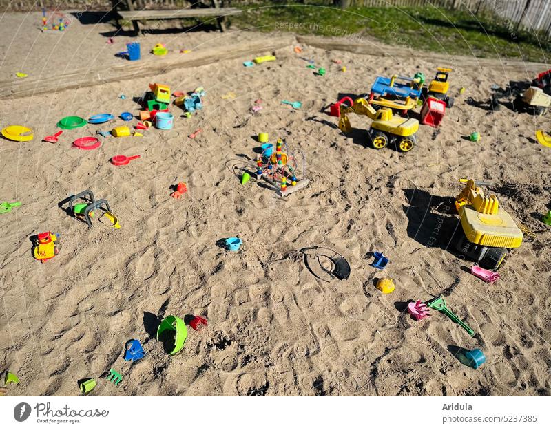 Verwaiste Sandkiste mit buntem Spielzeug Kindheit Plastik Kunststoff Schaufel Bagger Eimer Sieb Kinder Kindergarten Spielplatz Bank Förmchen Außenaufnahme