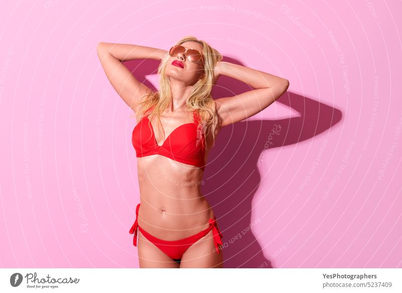 Frau in einem roten Badeanzug vor einem rosa Hintergrund. Blonde Frau in hellem Licht. 50s Strand Schönheit Bikini blond Körper BH Farbe Konzept cool Design