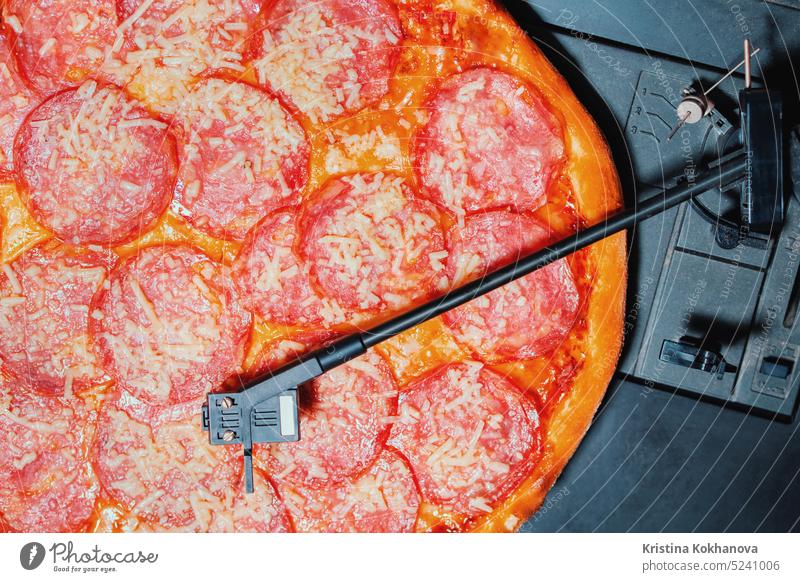 Italienische Pizza mit Salami als Schallplatte, die sich auf einem Plattenspieler dreht. Vinyl Musik Party Peperoni Lebensmittel Käse schnell heiß Scheibe