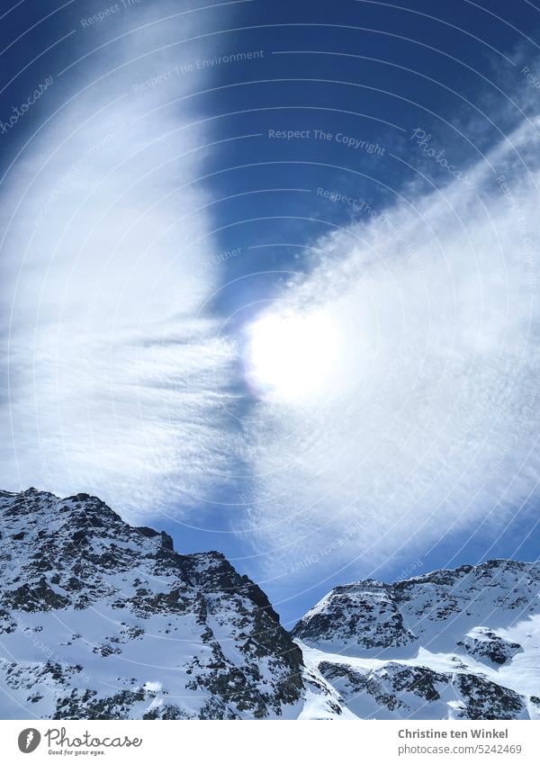 Der gleißende Sonnenball mit Wolkenflügeln schwebt über verschneiten Felsen Wolkenbild Himmel Luft Sonnenlicht Blauer Himmel Schönes Wetter Gegenlicht Umwelt