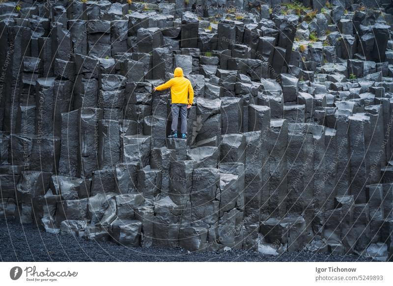 Mann in gelbem Mantel mit Blick auf die Reynisdrangar-Basaltsäulen am Reynisfjara-Strand, Island Küste Natur reisen isländisch Landschaft schwarzer Sand Felsen