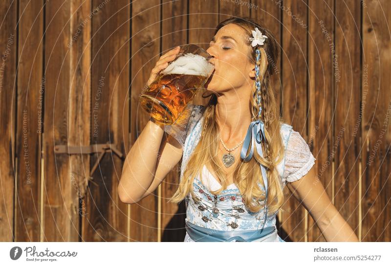Mädchen in traditioneller bayerischer Tracht trinkt Bier aus einem großen Krug im bayerischen Biergarten oder auf dem Oktoberfest Frau gold Party Restaurant