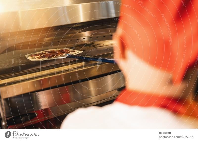 männlicher Koch schiebt eine rohe Pizza in den Steinofen in der italienischen Pizzeria Holzfeuer Ziegelofen Chefkoch Feinschmecker professionell Arbeit