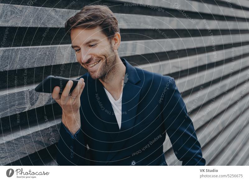 Junger attraktiver Mann steht im Freien und benutzt einen Spracherkennungsassistenten auf seinem Smartphone Mobile Telefon Geschäftsmann Freisprecheinrichtung