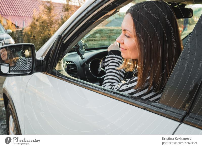 Glückliche Frau fährt weißes Auto, Dame lächelt, schaut in den Spiegel. Erfolgreiches Mädchen im Auto. PKW Fahrzeug Automobil Fahrer Erwachsener schön Transport