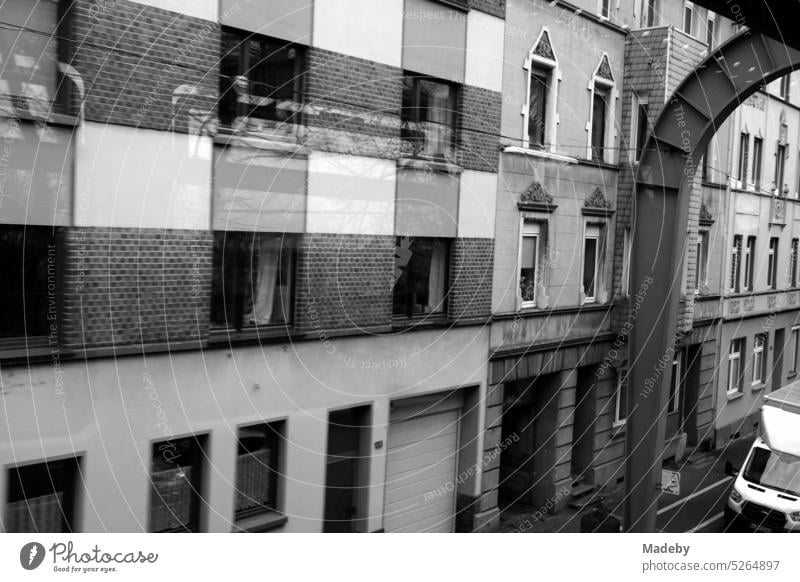 Graue Fassaden der alten Häuser entlang der Streckenführung der Wuppertaler Schwebebahn bei Regenwetter im Stadtteil Vohwinkel in Wuppertal im Bergischen Land in neorealistischem Schwarzweiß