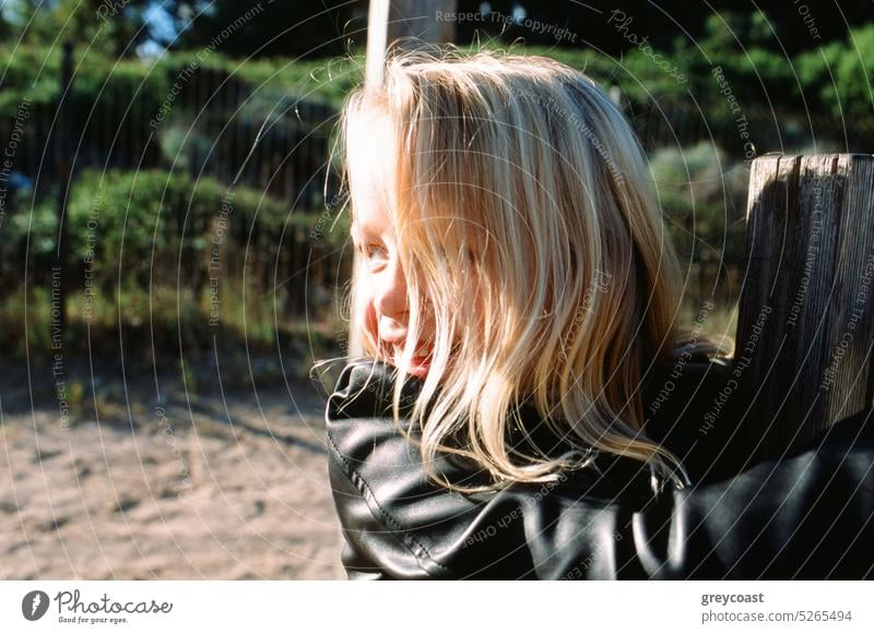 Kleines Mädchen klettert an einem sonnigen Tag auf einen Zaun Kind Aufstieg Landschaft lustig Spaß haben ländlich Kindheit heiter Lächeln Lederjacke Natur Stil