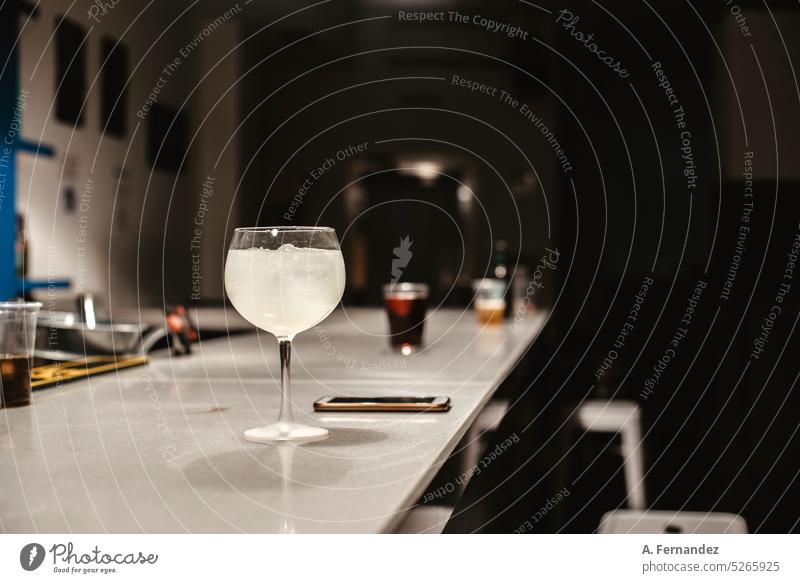 Ein Cocktail, der in einem Ballonglas auf einem Bartresen neben einem Mobiltelefon serviert wird. Cocktailbar Theke Abfertigungsschalter Hintergrund Nachtleben