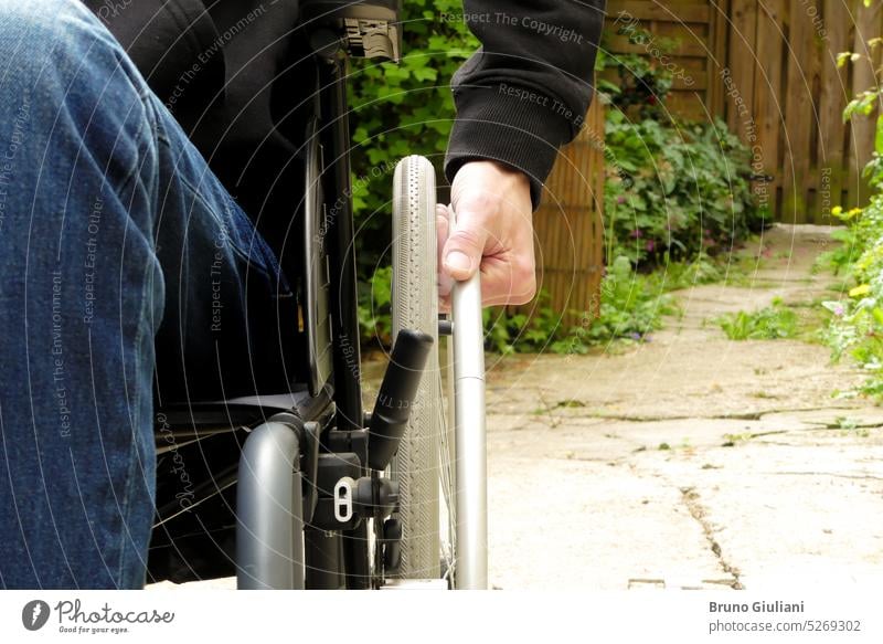 Eine behinderte Person in einem Rollstuhl. Ein Mann mit eingeschränkter Mobilität in einer begrünten Gasse. allein Behinderungen im Freien Hand Rad abschließen