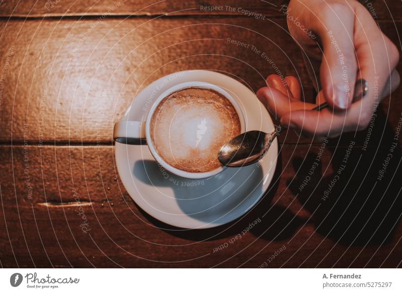 Männliche Hand hält einen kleinen Löffel neben einer Tasse Kaffee, von oben gesehen Kaffeepause Kaffeetasse Kaffeehaus Kaffeebecher männlich Mann Beteiligung