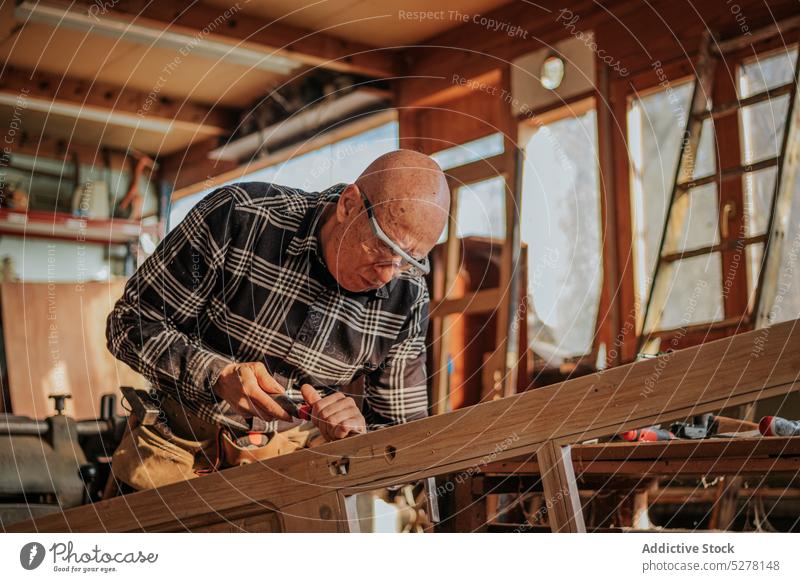 Älterer Schreiner beim Meißeln in der Werkstatt Mann Beitel Tischlerin geschnitten Kunsthandwerker Schiffsplanken Holz Fähigkeit Kunstgewerbler Schreinerei