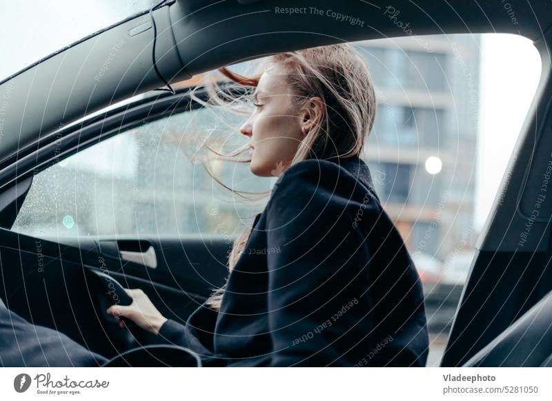 Frau in schwarzem Mantel steigt in der Stadt aus dem Auto. Windiges Wetter, wehende Haare PKW Frauen rauskommen Taxi reisen blasend Reise Lifestyle Erholung
