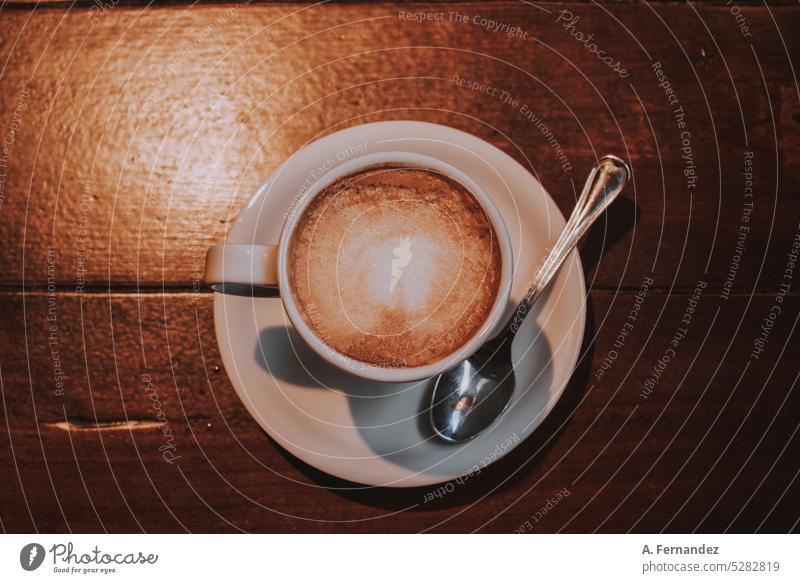 Eine Tasse Kaffee mit einem kleinen Teelöffel auf einem Holztisch Kaffeelöffel Tisch hölzern Holzbrett Teelöffel. Kaffeelöffel Café Kantine Milchkaffee