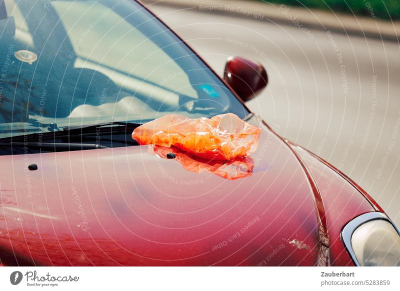 Orange Plastiktüte auf Motorhaube eines roten Autos orange Müll Stadt Mobilität Klima Umwelt Vergangenheit Erdöl Schwung Linie Ästhetik Glanz Kunststoff