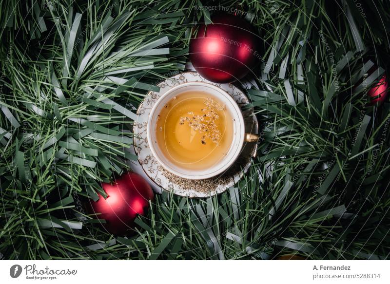 Teetasse gefüllt mit Kräutertee, umgeben von Lametta und zwei roten Weihnachtskugeln Tasse Kräuterbuch Weihnachten Weihnachtsflitter Weihnachtsball