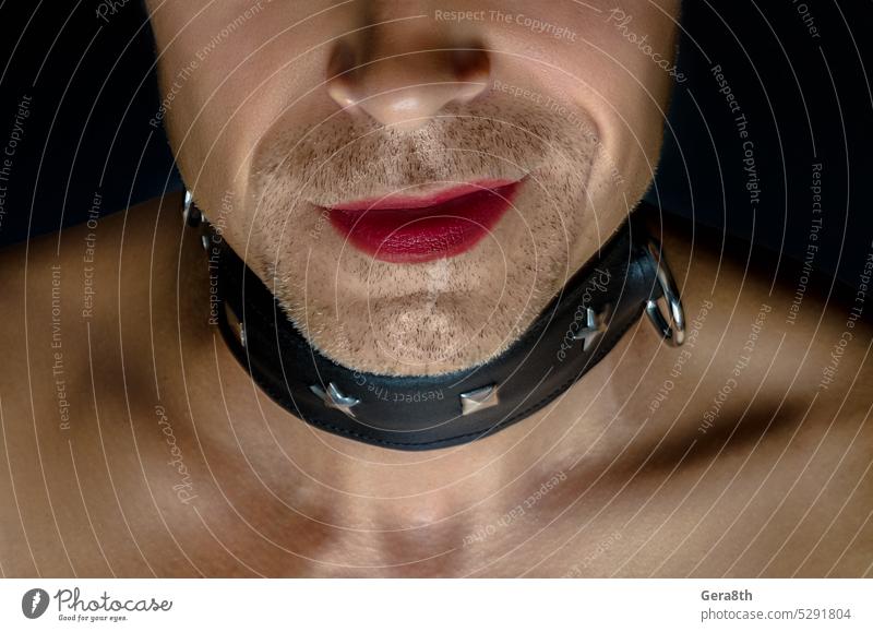 Mann mit BDSM-Halsband lächelt, seine Lippen sind mit rotem Lippenstift bemalt lgbt+ Junge Kragen Vor dunklem Hintergrund schwul Geschlecht grinsen menschlich