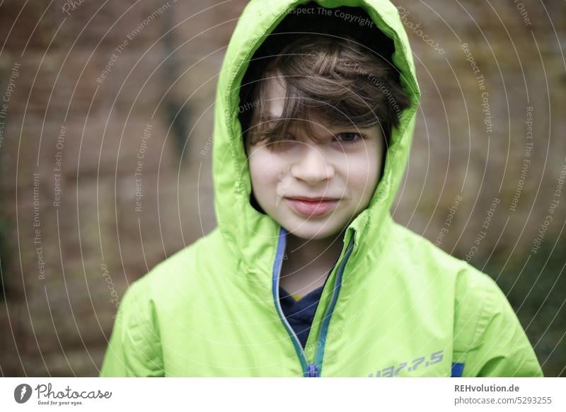 Kind mit Kapuze Mensch Junge Kindheit Umwelt Jacke Mütze Lächeln natürlich Blick in die Kamera Porträt Oberkörper Tag Zentralperspektive Außenaufnahme