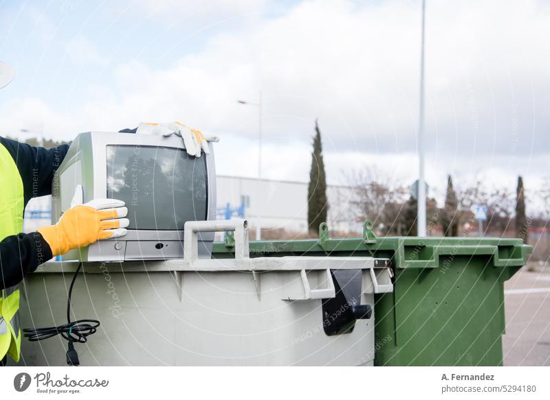 Ein Arbeiter in einer Recyclinganlage hält einen alten Fernseher neben einem Mülleimer. Technologie-Recycling-Konzept. Abfallwirtschaft wiederverwerten