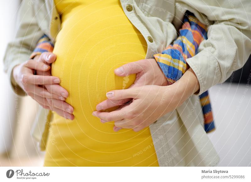 Junger Mann hält Hände auf schwangeren Bauch seiner Frau jung Paar Zukunft Eltern abschließen Nahaufnahme aufbewahren Magen Pflege Umarmung unkenntlich Umarmen