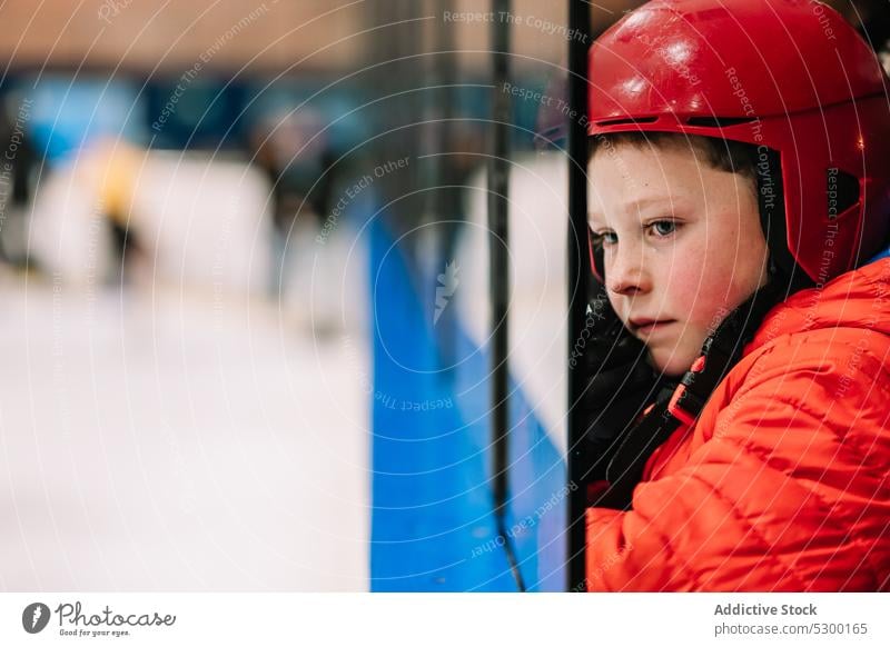 Nachdenklicher Junge mit Blick auf die Eislaufbahn Winter Kind Sicherheit nachdenklich Zaun behüten kalt besinnlich ernst Schutzhelm Saison Aktivität Sport