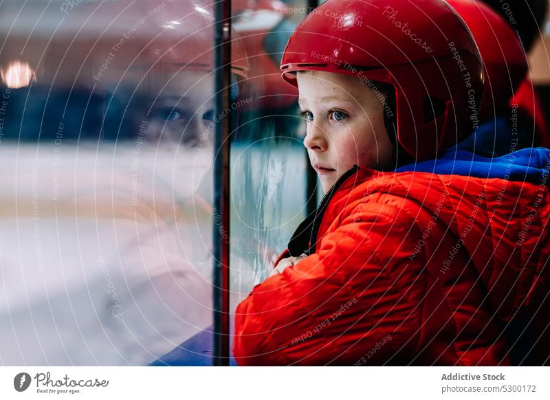 Nachdenklicher Junge mit Blick auf die Eislaufbahn Winter Kind Sicherheit nachdenklich Zaun behüten kalt besinnlich ernst Schutzhelm Saison Aktivität Sport